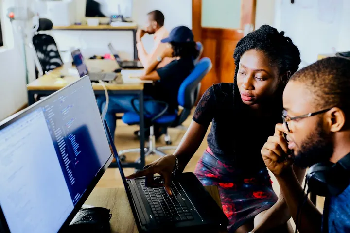 Dos personas revisando código y datos en una pantalla en una oficina