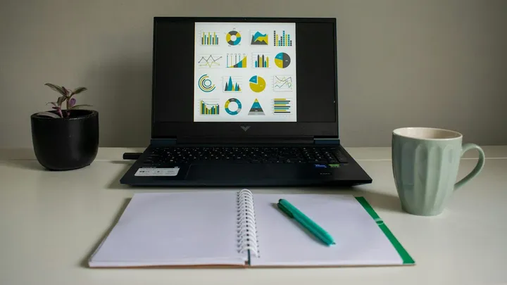 Laptop mostrando gráficos junto a una libreta y una taza